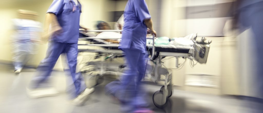 Lääkäri ja hoitajat työntävät sairaalasänkyä vauhdikkaasti. 