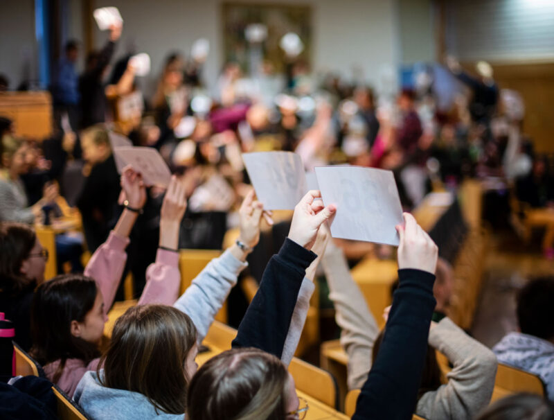 Unga samlade i auditorium sträcker upp numrerade lappar i omröstning.